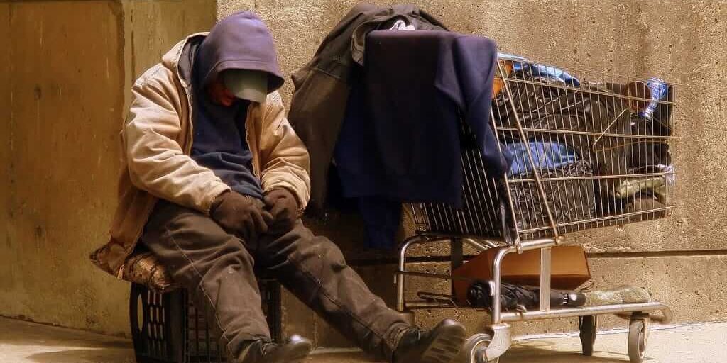 homeless man homeless man sitting next to a grocery cart filled with his possessions