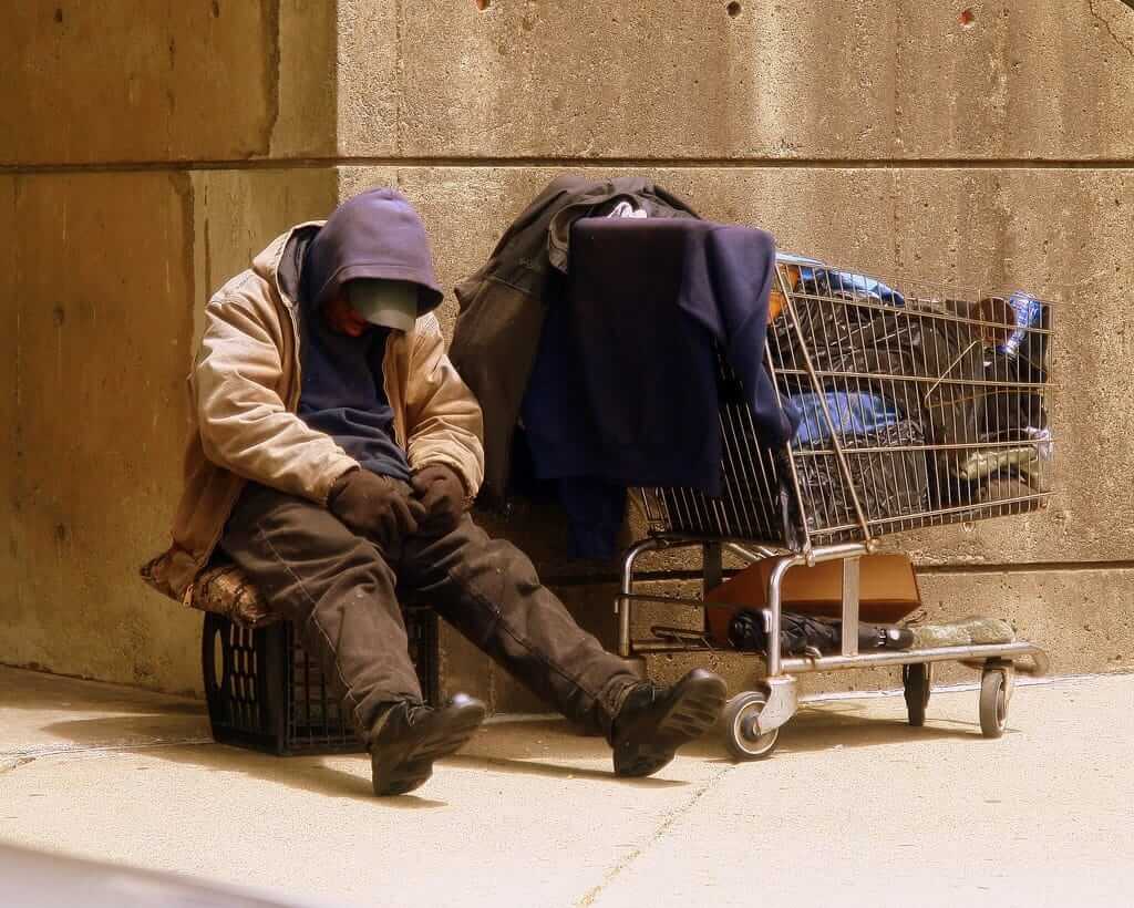homeless man homeless man sitting next to a grocery cart filled with his possessions