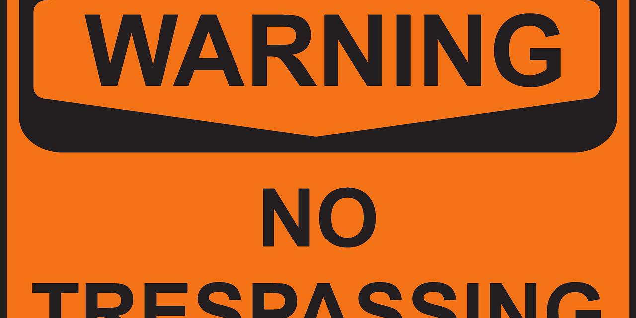 orange sign with black text that says warning, no trespassing