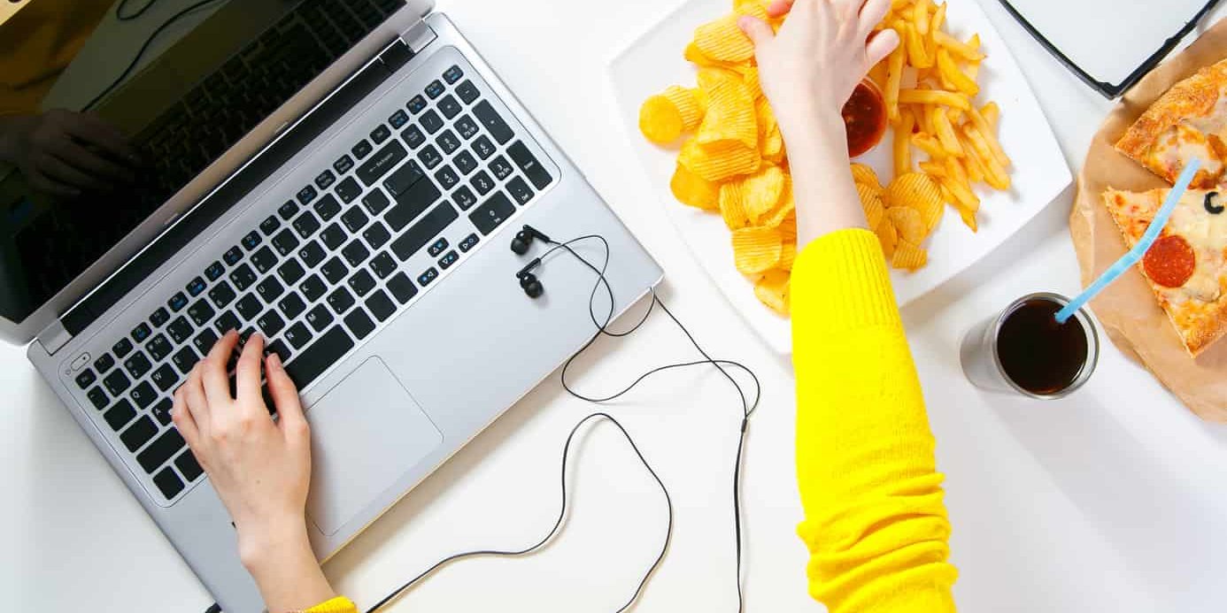 a lady typing on her computer and eating potato chips