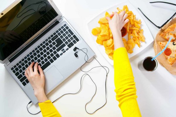 a lady typing on her computer and eating potato chips